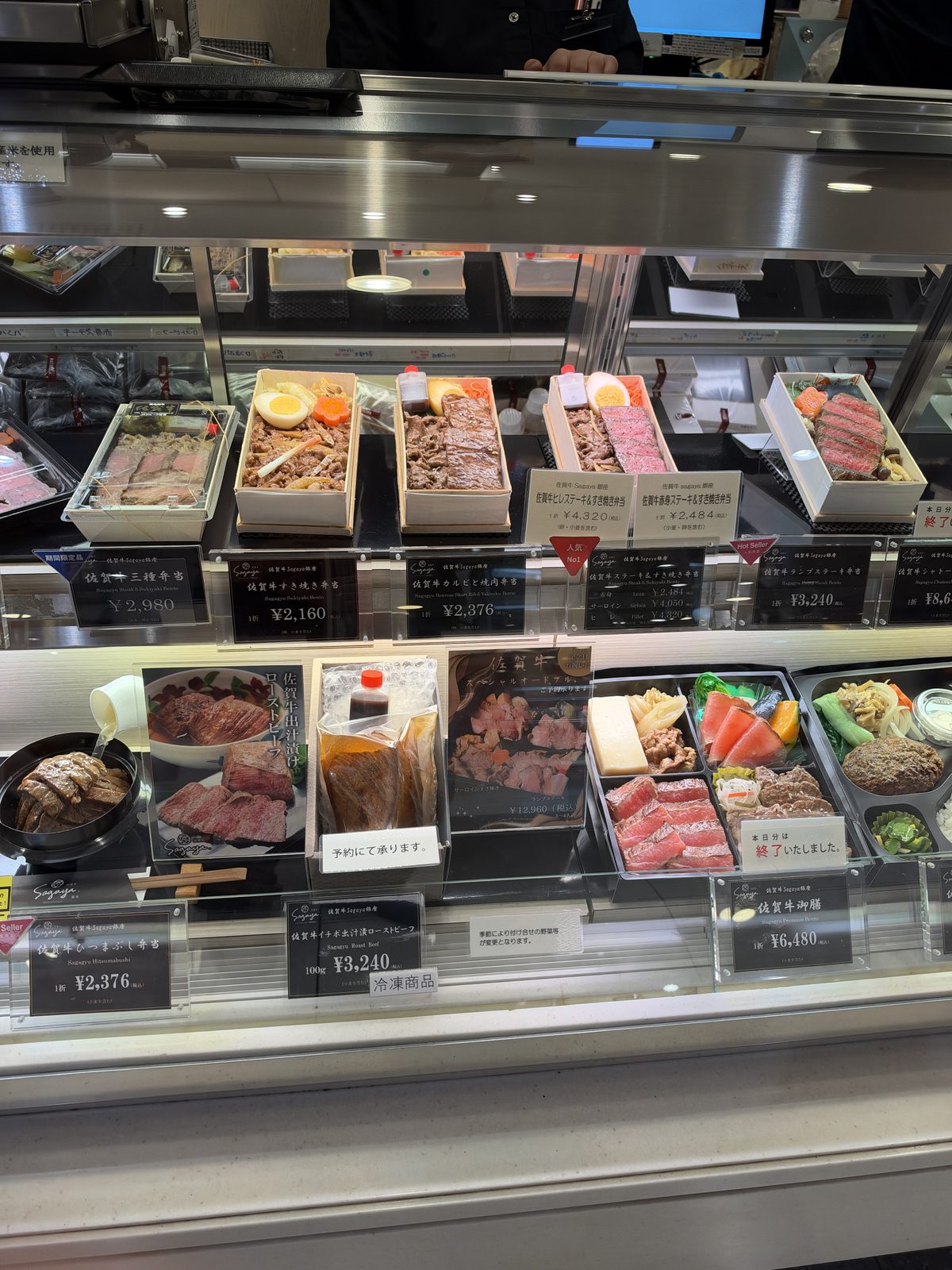 A bento counter in a department store food hall, with prices on each box, photographed in October 2026.