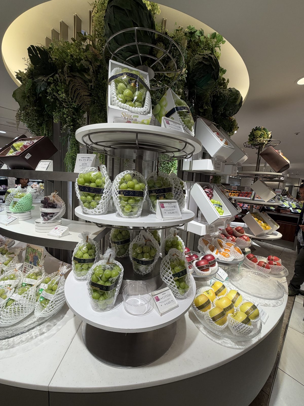 A tiered fruit display with individually wrapped grapes, photographed in October 2026.