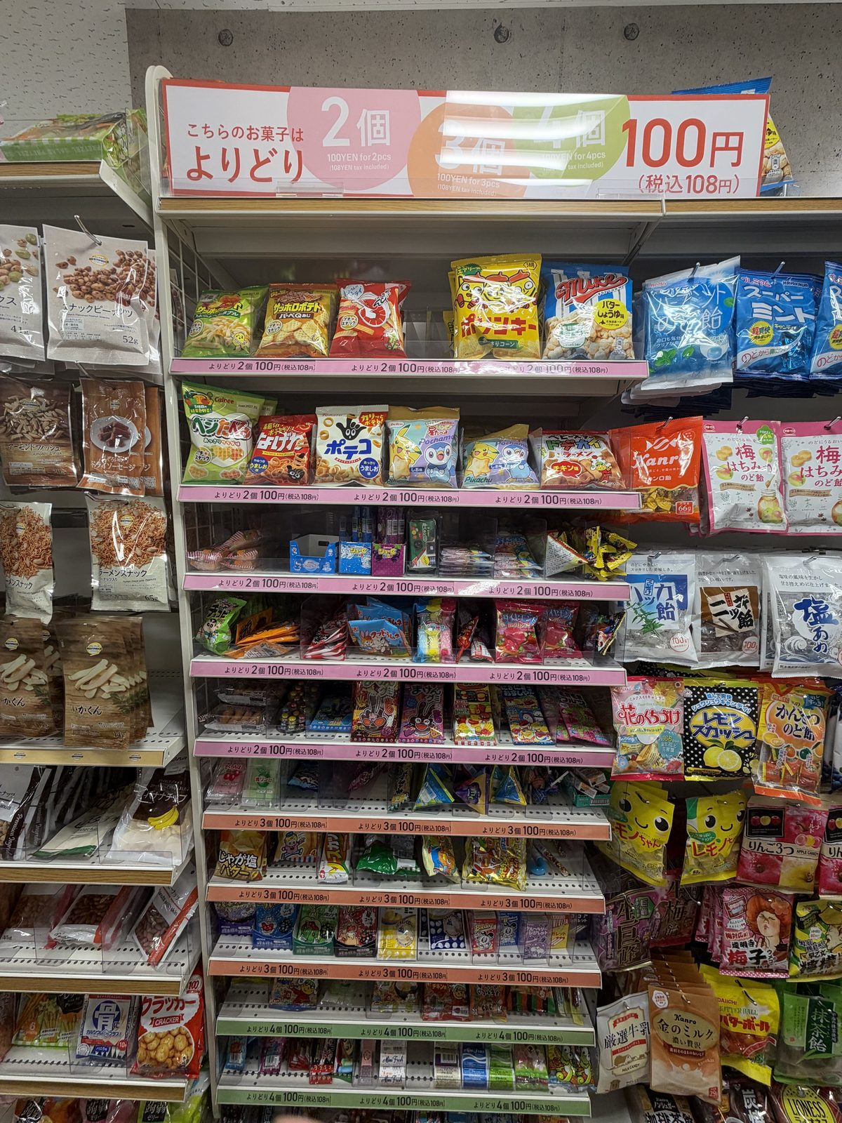 The snack aisle. The sign reads 100 yen, 108 yen including tax, for two of the marked items.